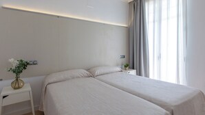 Una habitación de hotel con dos camas, una mesita de noche con un jarrón de flores y una ventana con cortinas.