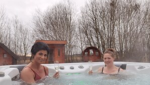 Two people in a hot tub with a wooden cabin and leafless trees in the background. - PAGA Hotel (Aidenbach)