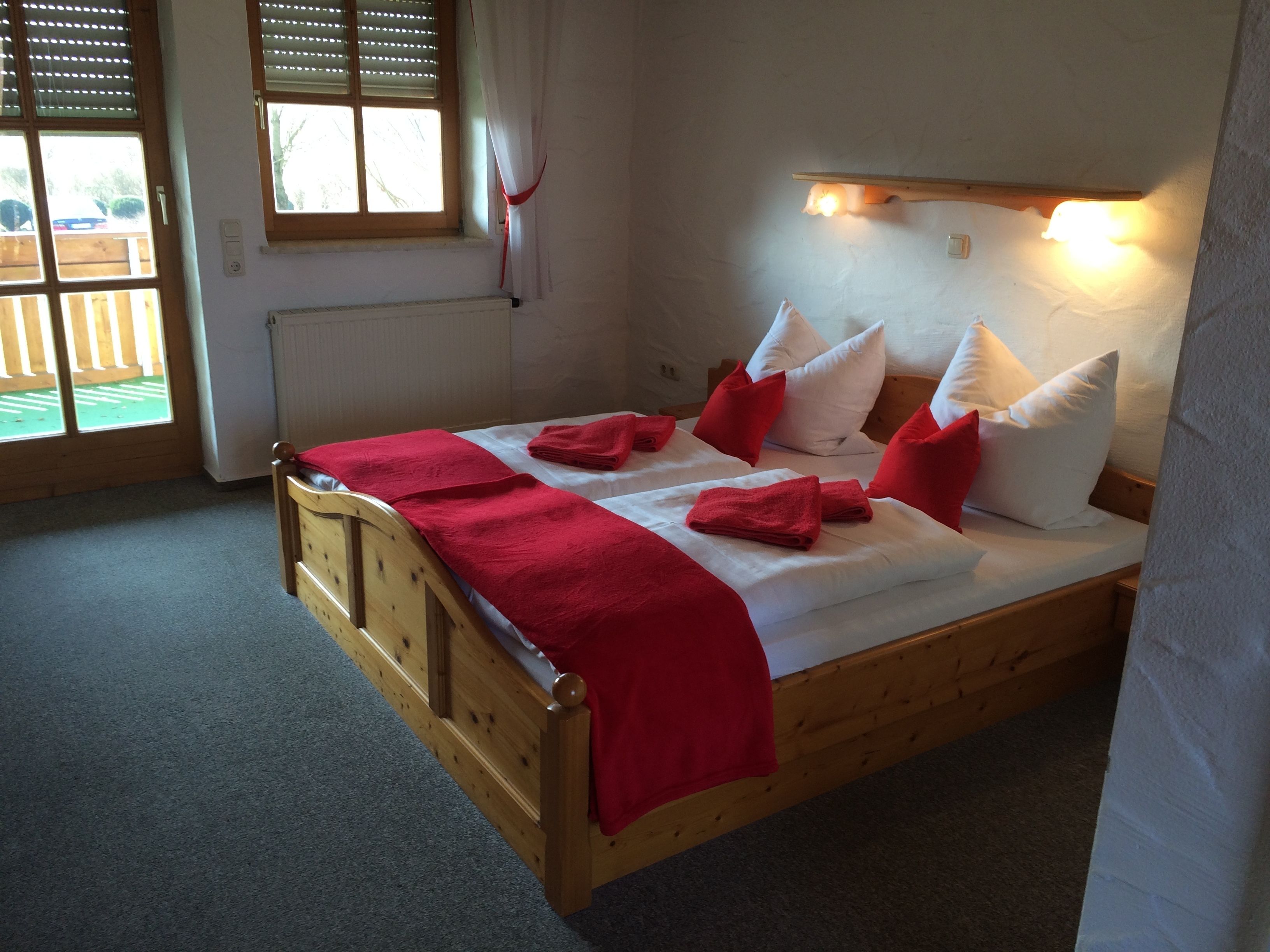 Una cama de madera con ropa de cama roja y blanca, un plaid rojo y almohadas.