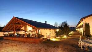 A building with a wooden deck and outdoor seating area, surrounded by trees and a gravel path. - PAGA Hotel (Aidenbach)