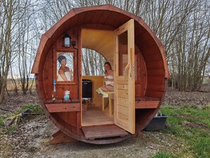 Une structure sphérique en bois, dotée d’une porte ouverte, laissant apercevoir une personne à l’intérieur.