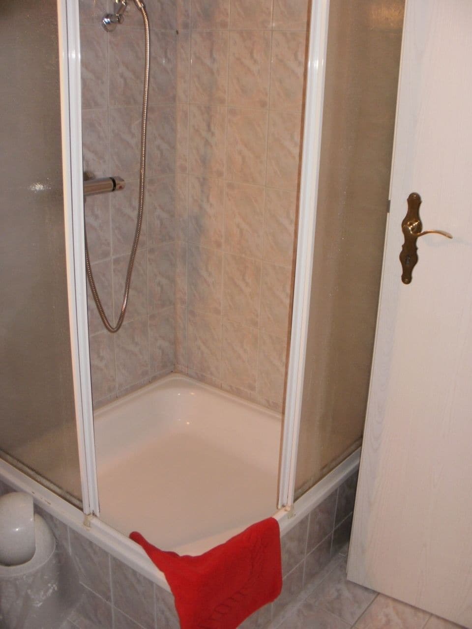 Cabina de ducha con puerta de vidrio, un cabezal de ducha y una bañera blanca.