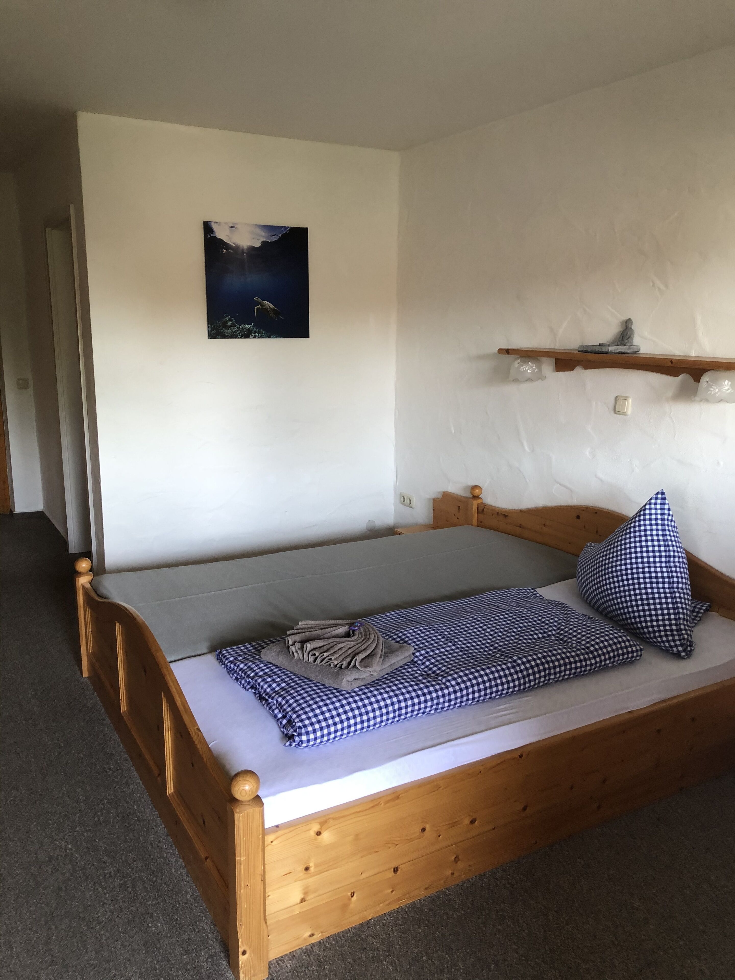 Habitación individual con cama de madera, colchón gris y manta azul a cuadros.