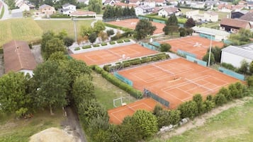 Vista aérea de un complejo de canchas de tenis con varias canchas, rodeado de edificios residenciales y áreas verdes.