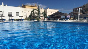Una piscina con agua azul cristalina, rodeada de sillas de descanso y sombrillas.