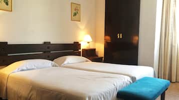 Een hotelkamer met twee bedden, een bankje, een nachtkastje met lamp en een kledingkast.
