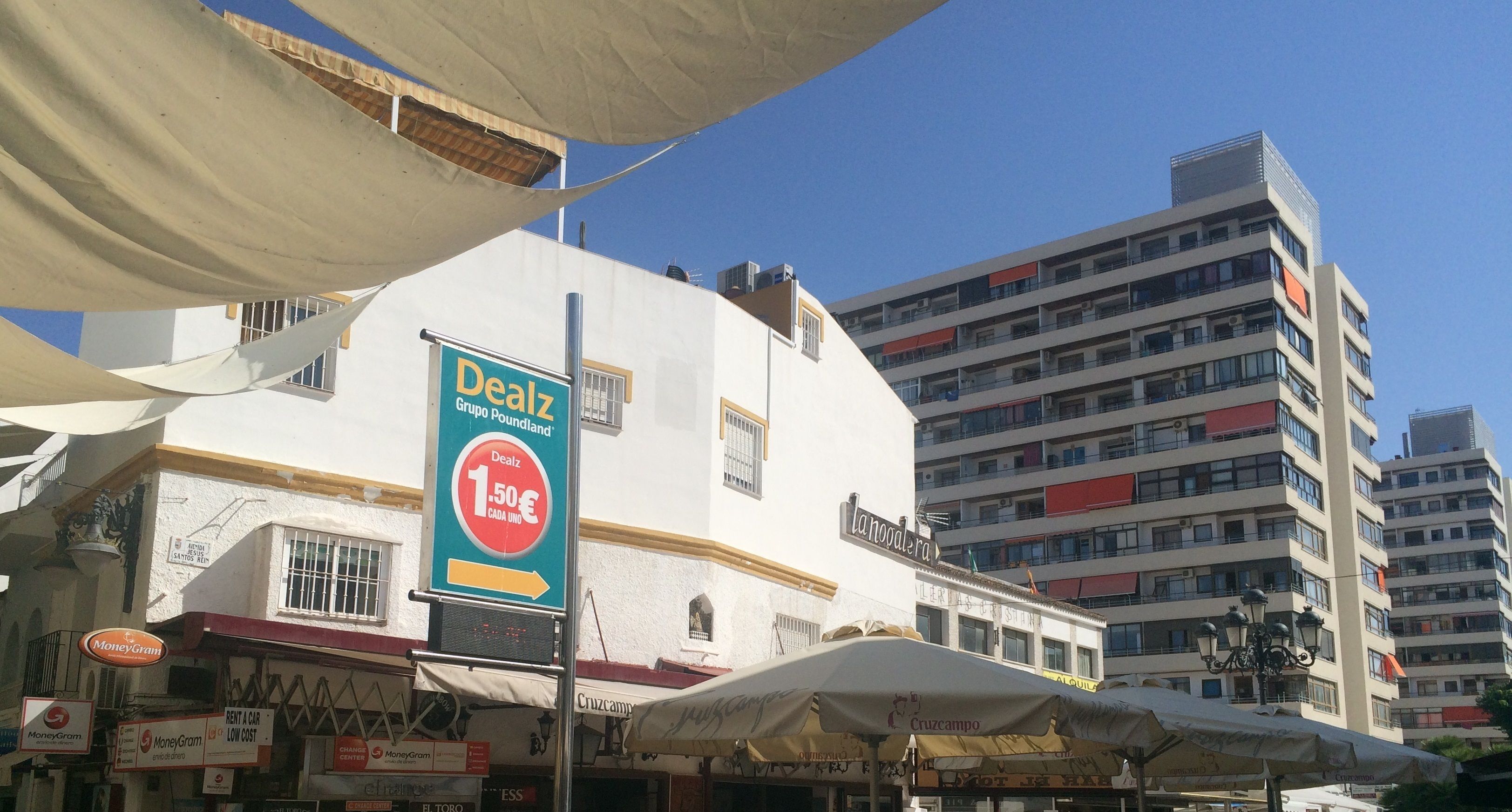 Un bâtiment avec une enseigne annonçant une promotion, un distributeur automatique de MoneyGram et un parapluie de la marque Cruzcampo.