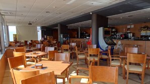 A spacious indoor dining area with wooden tables and chairs, a bar area with a counter and various items, and a large pillar. - Hotel Las Terrazas (Albolote)