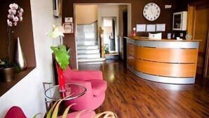 A reception area with a wooden reception desk, a clock, and a red chair. - Hotel Las Terrazas (Albolote)
