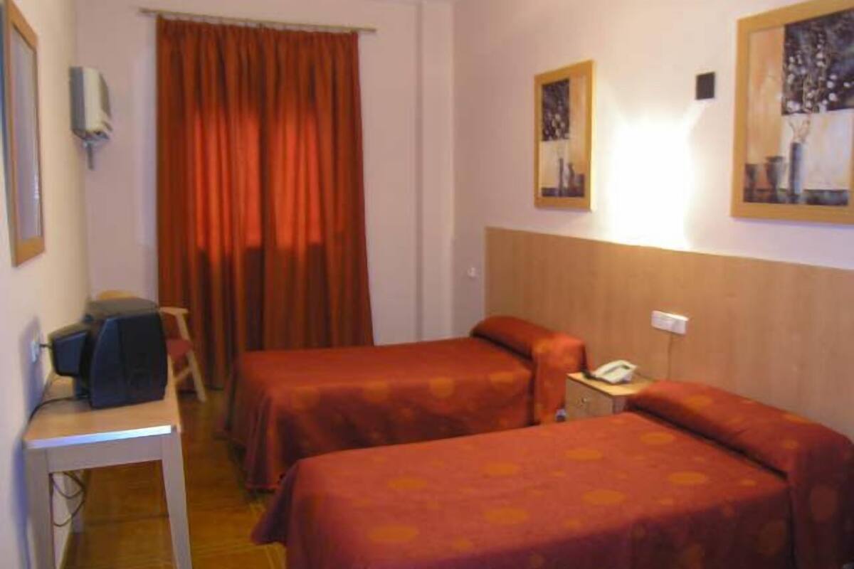 A hotel room with two beds, a desk, a chair, a telephone, and a window with curtains.