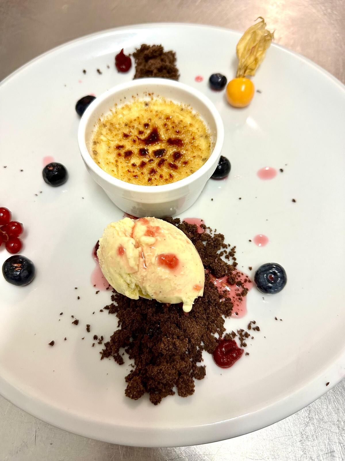 En desserttallrik med crème brûlée, glass och bär.