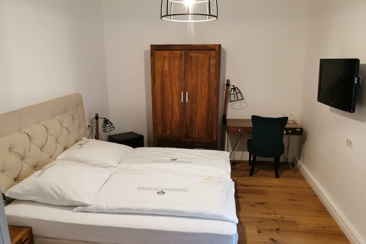 Une chambre à coucher avec un lit, une armoire en bois, un bureau, une chaise et un téléviseur fixé au mur.