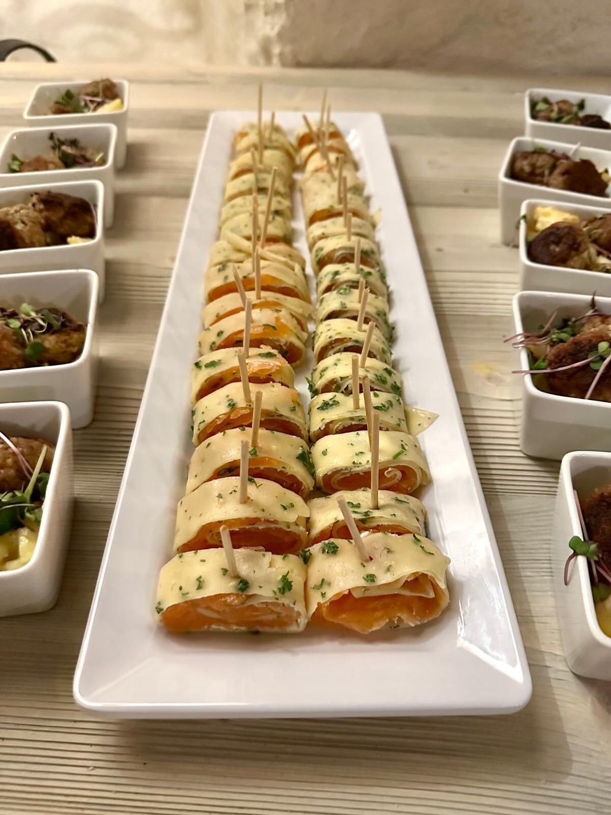 A white rectangular plate with rolled appetizers arranged in a row, each held together with toothpicks.
