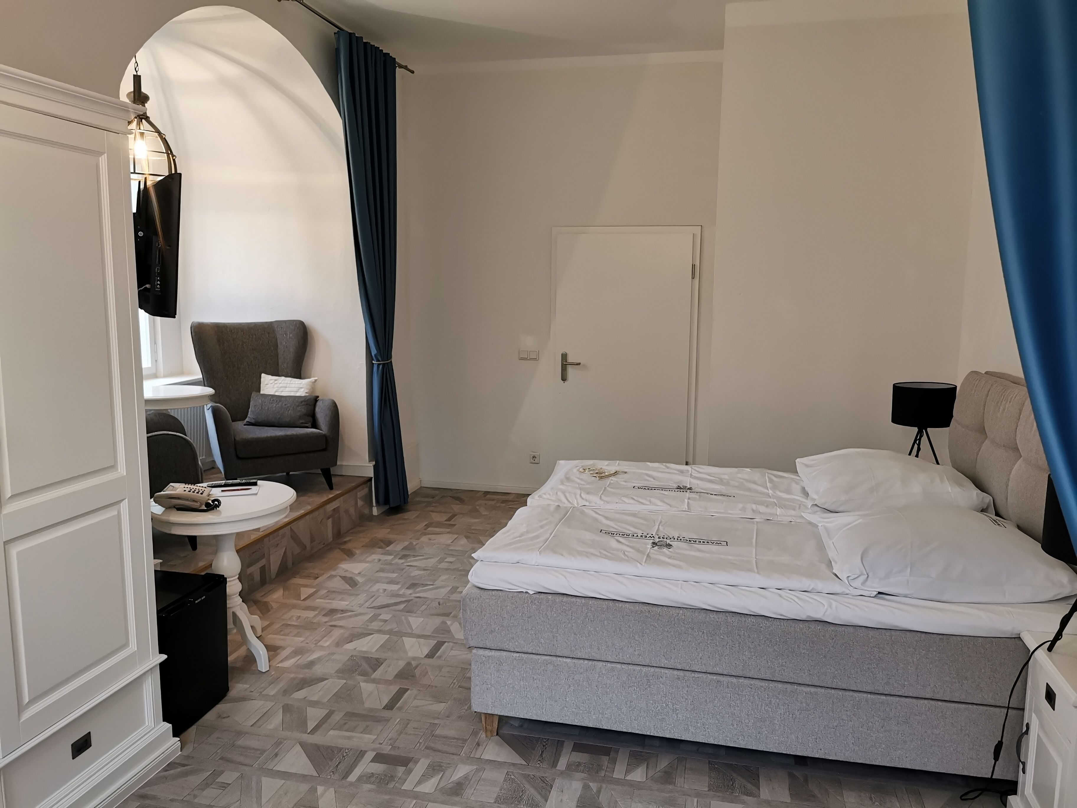 A bedroom with a bed, a chair, a desk, and a wardrobe.