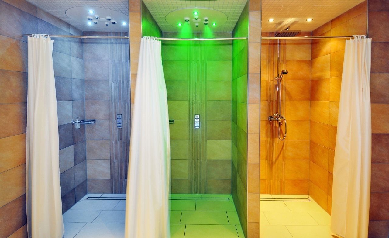 A modern bathroom with three shower areas, each with a different colored lighting and tiled walls.