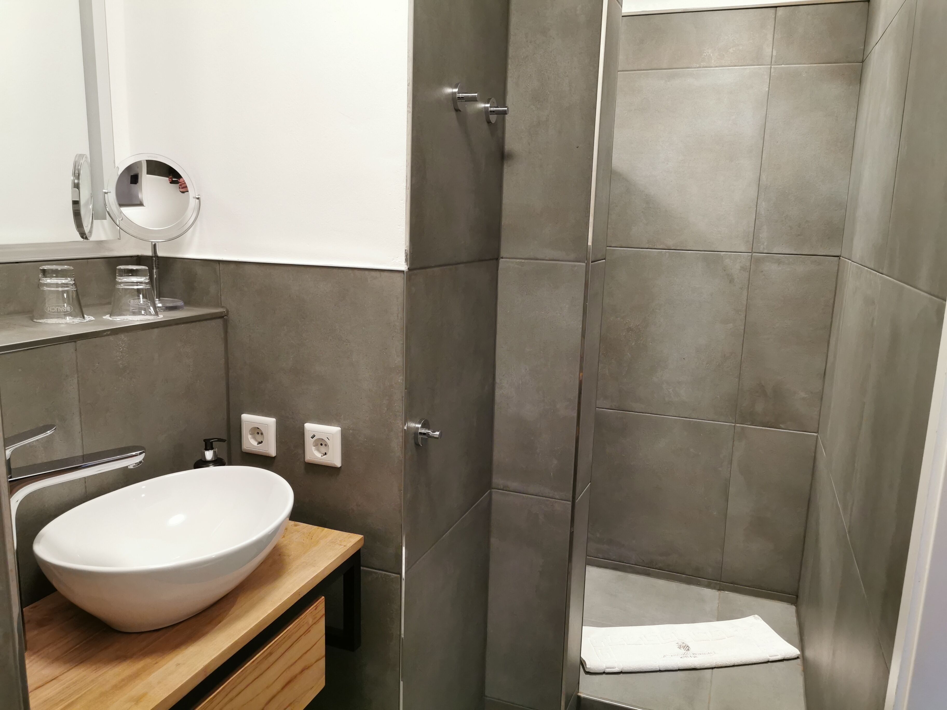 Ein modernes Badezimmer mit einem großen, weißen Waschbecken, einem Spiegel und einer Duschkabine.