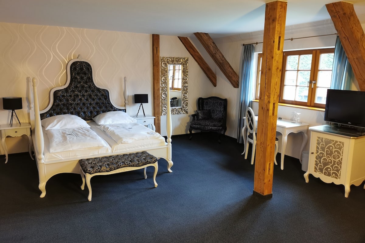 Une chambre à coucher avec un lit à baldaquin, un bureau avec une télévision, une chaise et une petite table.