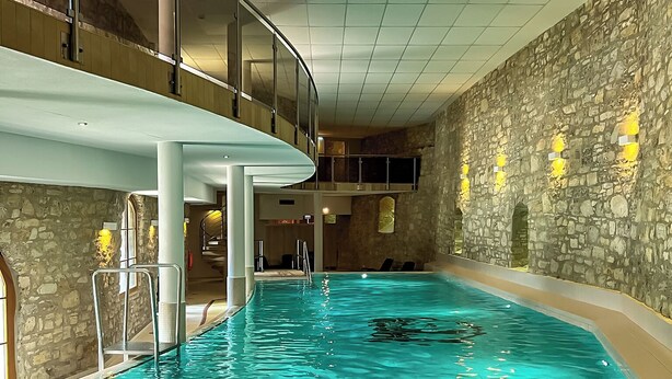 Une piscine intérieure avec un mur en pierre et une balustrade en verre.