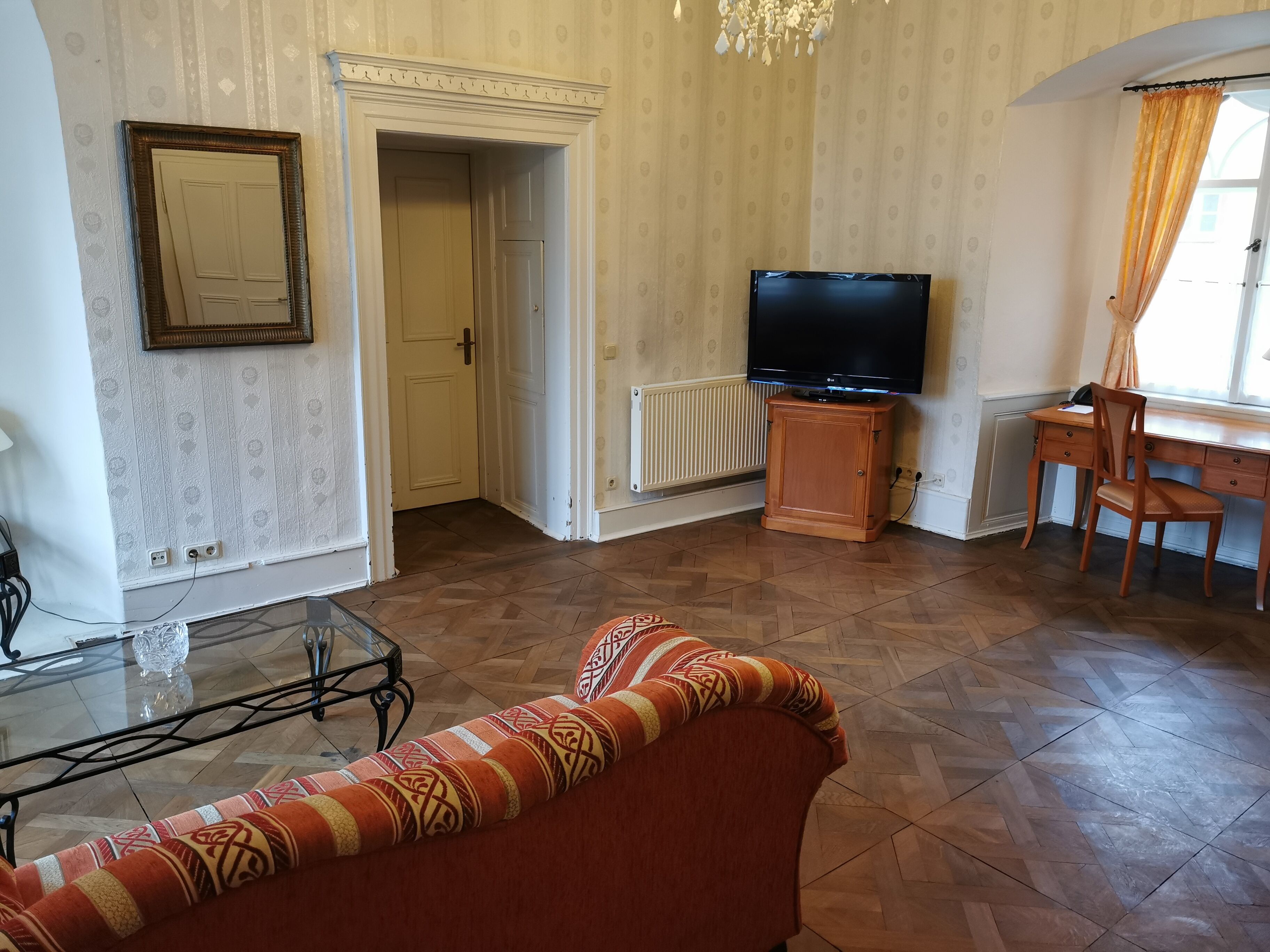 Una sala de estar con un sofá, una mesa de centro de vidrio, un televisor, un mueble de madera y un escritorio con una silla.