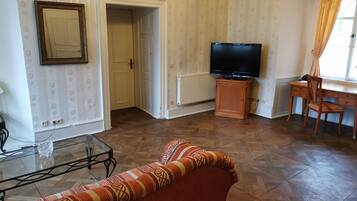 Una sala de estar con un sofá, una mesa de centro de vidrio, un televisor, un mueble de madera y un escritorio con una silla.