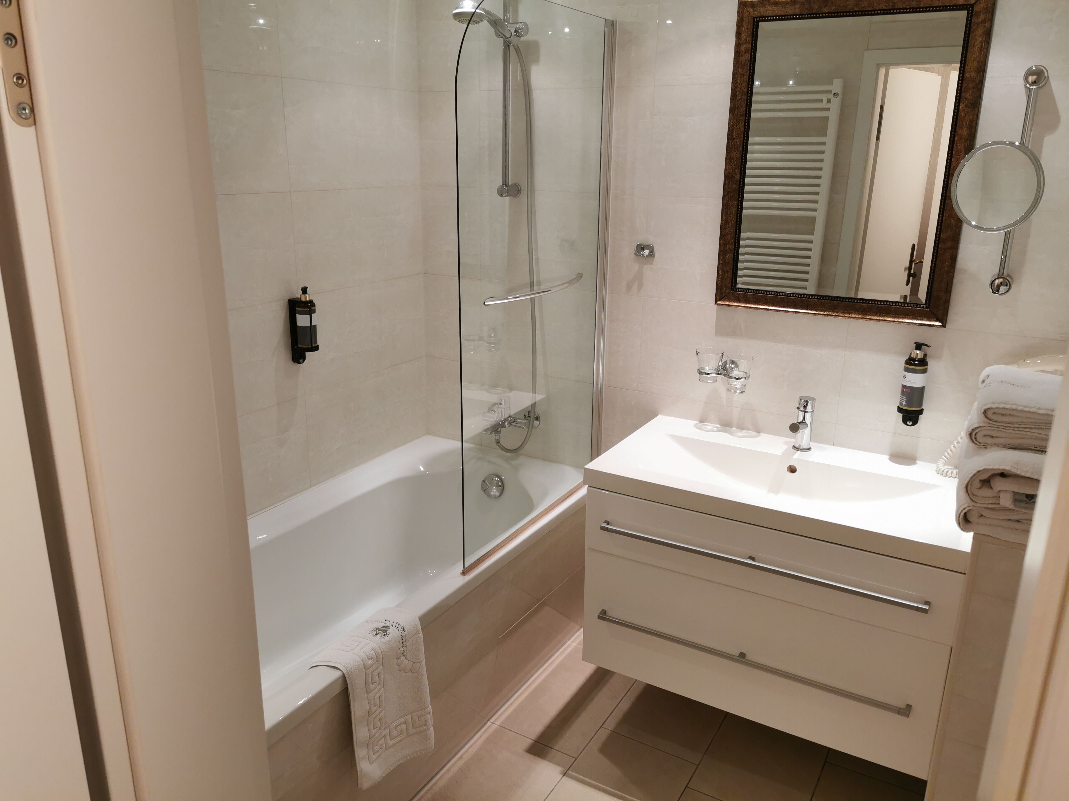 Une salle de bain moderne avec une douche à parois de verre, une baignoire blanche, un meuble-lavabo avec un miroir et des serviettes soigneusement pliées.