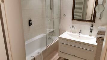 Une salle de bain moderne avec une douche à parois de verre, une baignoire blanche, un meuble-lavabo avec un miroir et des serviettes soigneusement pliées.