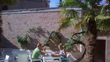 Een terras met witte stoelen en tafels, een bakstenen muur en een palmboom.