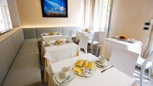 Een restaurantgedeelte van een hotel met een lange bank en meerdere tafels, elk met borden eten, bekers en bestek.