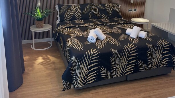 Een moderne slaapkamer met een groot bed, twee wandlampen, een klein rond tafeltje en twee ingekaderde foto's.
