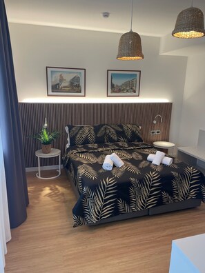 Une chambre moderne avec un grand lit, deux lampes fixées au mur, une petite table ronde et deux tableaux encadrés.