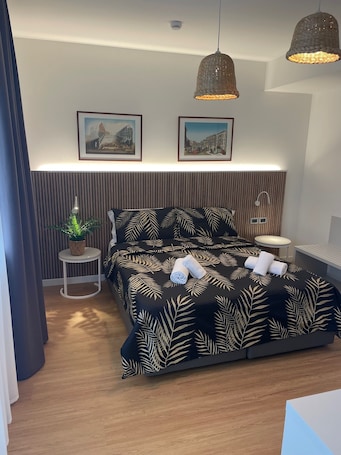 A modern bedroom with a large bed, two wall-mounted lamps, a small round table, and two framed pictures.