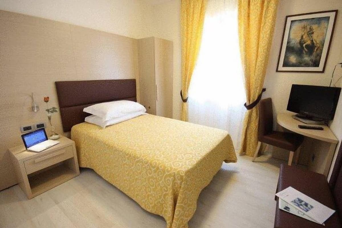 Une chambre d’hôtel avec un lit, un bureau, une chaise, une télévision et un ordinateur portable posé sur la table de chevet.