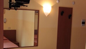 A compact room with a desk, chair, and a small refrigerator. A mirror and a wall-mounted light are also visible. - Soggiorno Comfort (Rome)