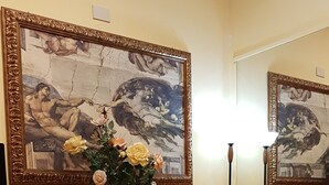 A room with two red leather chairs, a vase with yellow flowers on a glass table, and two large framed paintings on the wall. - Soggiorno Comfort (Rome)