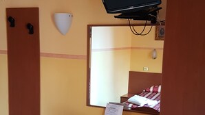 A compact hotel room with a bed, a desk with a chair, a small refrigerator, an air conditioner, a television, and a mirror. - Soggiorno Comfort (Rome)