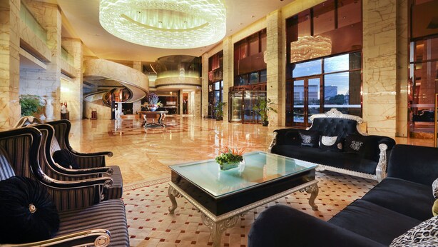 A spacious lobby with a grand chandelier, a black sofa, and a glass coffee table. - Royal International Hotel (Shanghai)