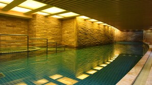A swimming pool with a tiled floor and walls, surrounded by stone walls and wooden beams. - Royal International Hotel (Shanghai)