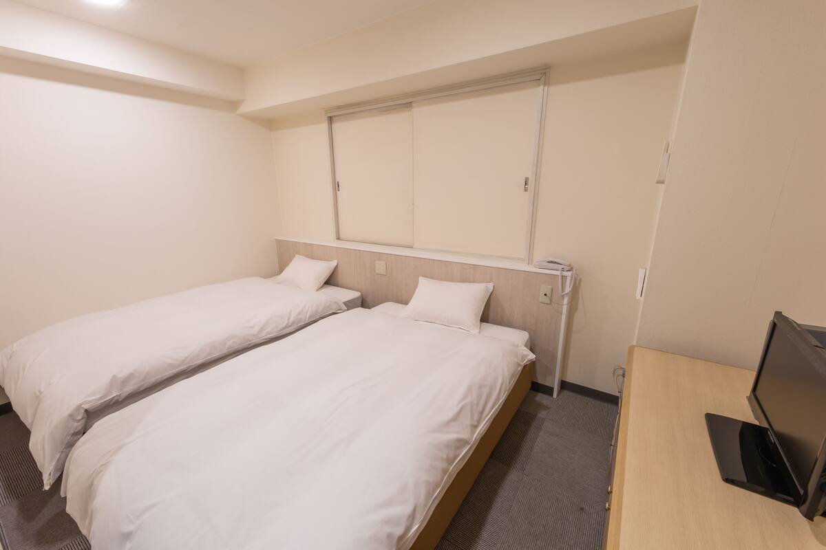 A hotel room with two single beds, a desk with a computer, and a sliding door closet.