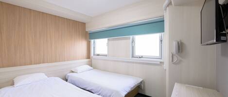 A hotel room with two single beds, a window with a view, a flat-screen TV mounted on the wall, and a ceiling light.