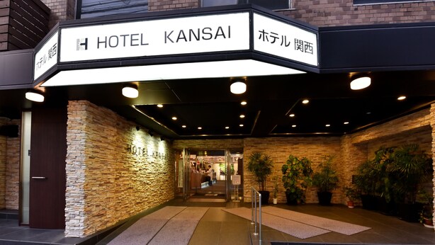 Exterior do Hotel Kansai, com fachada de pedra, entrada e vasos de plantas.