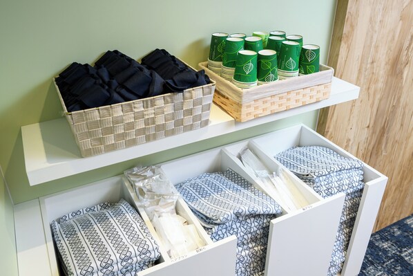 Una exhibición de textiles negros y azules con diseños ordenados en estantes, junto a latas con motivos de hojas verdes.