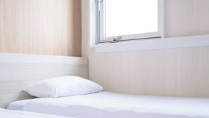 Uma cama bem arrumada com lençóis e almofadas brancas, uma cabeceira de madeira e uma janela com persianas.