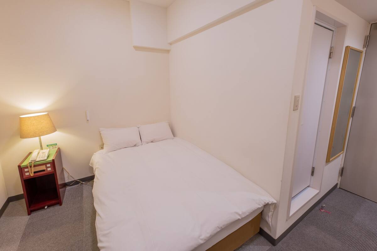 A hotel room with a single bed, a bedside table with a lamp, and a door.