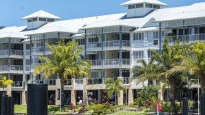 A multi-story hotel with balconies, a garden area with palm trees, and a clear blue sky.