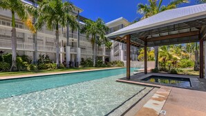 A swimming pool with clear water, surrounded by palm trees and a covered pavilion.