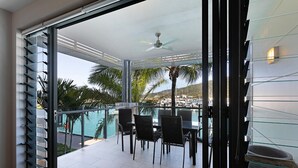 A balcony with a glass railing, a ceiling fan, and a view of a pool and palm trees.