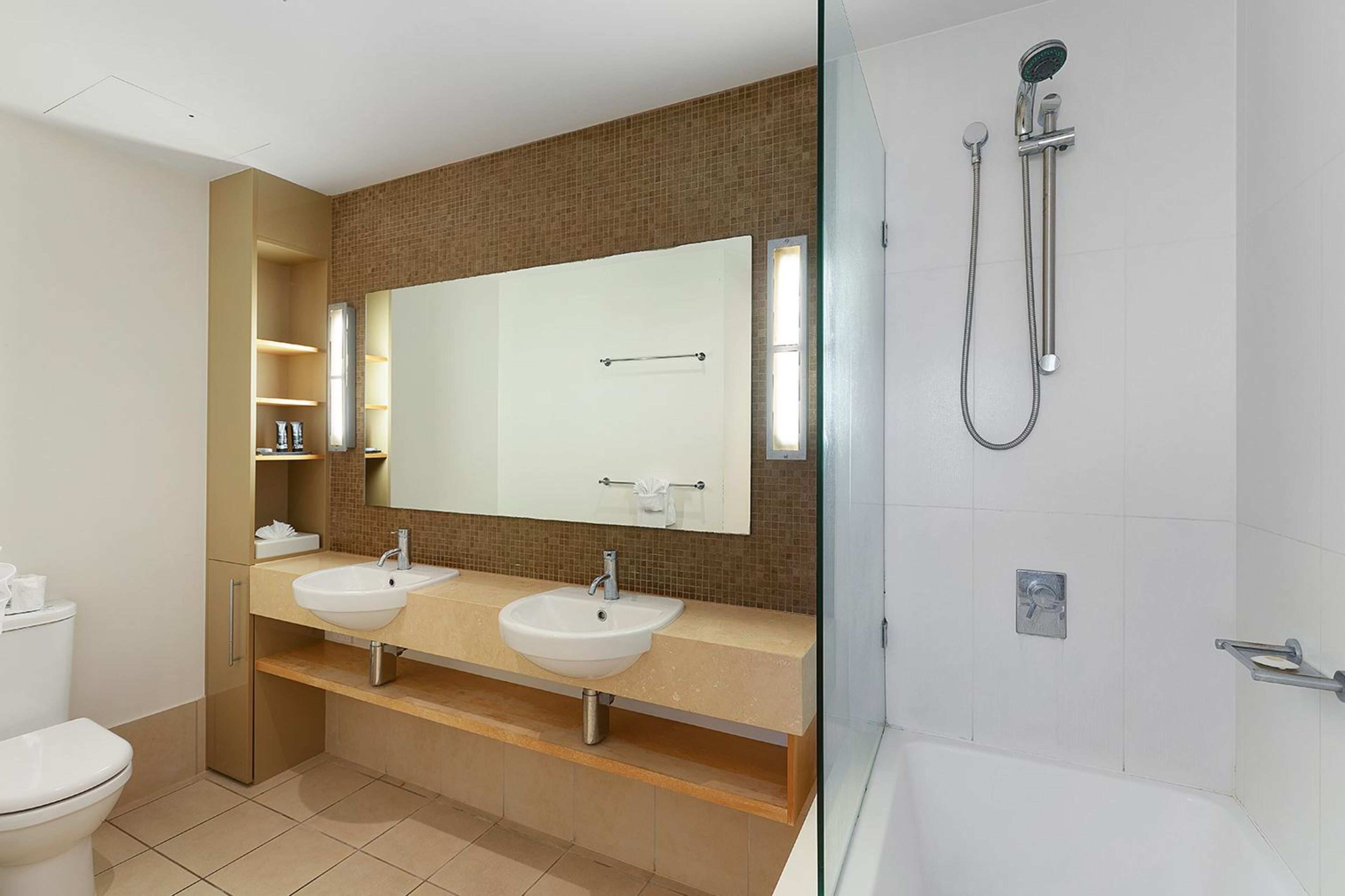 A modern bathroom with two sinks, a large mirror, and a shower.