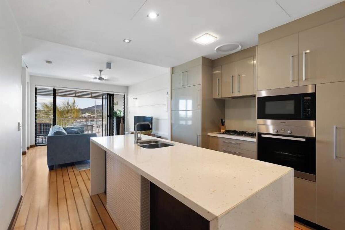 Una cocina moderna con una isla central, electrodomésticos de acero inoxidable y vistas a un balcón exterior.