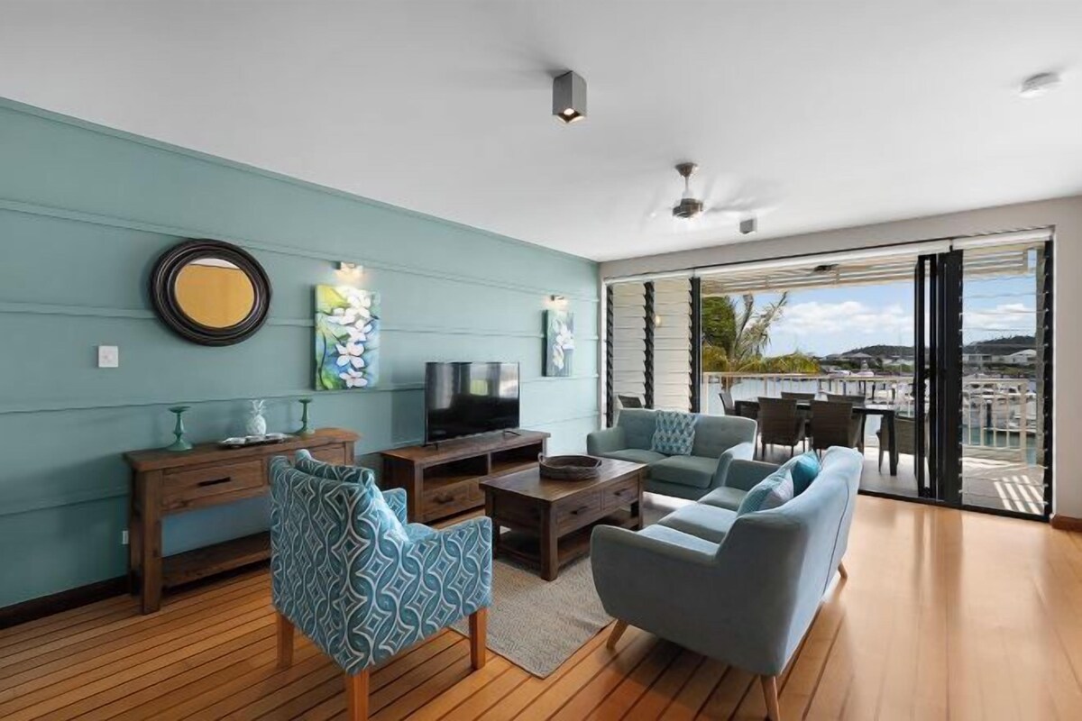 Una sala de estar moderna con piso de madera, paredes color turquesa y un balcón con vista a la ciudad.