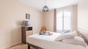 Ein Hotelzimmer mit Bett, Fernseher auf einer Holzkommode, einem Sessel und einem Fenster mit Vorhängen.